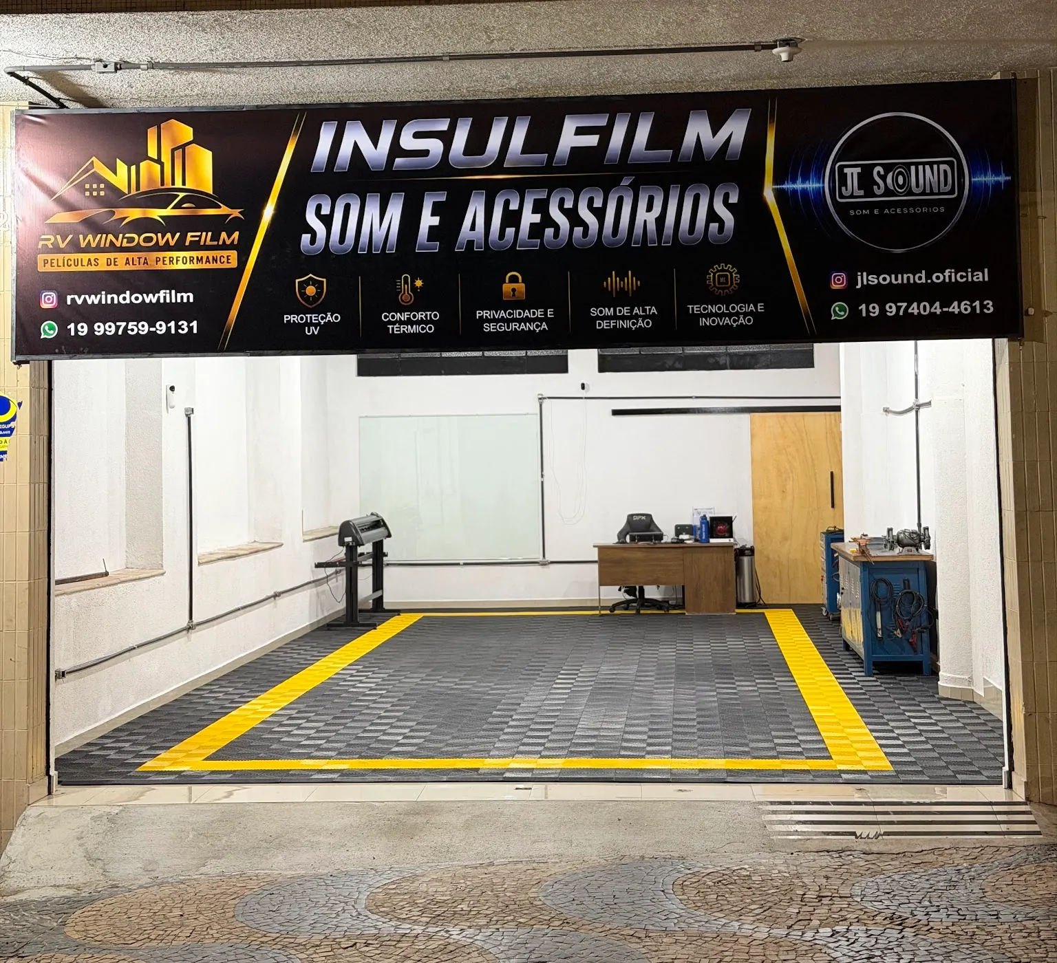 Fachada da loja da RV Window Film à noite, com a placa e o box de aplicação iluminado, na Avenida Andrade Neves, em Campinas